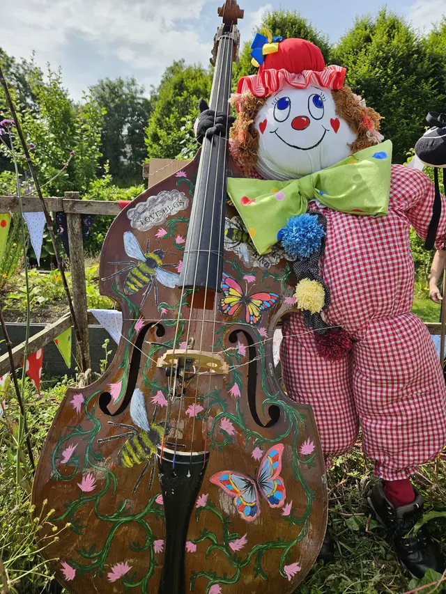 A colourful clown scarecrow beside a hand-painted double bass